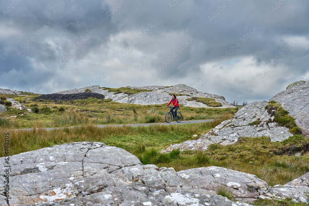 nice senior woman on mountain bike, cycling in the rough karst landscape of Burren near Ballyvaughan, County Clare in the western part of the Republic of Ireland