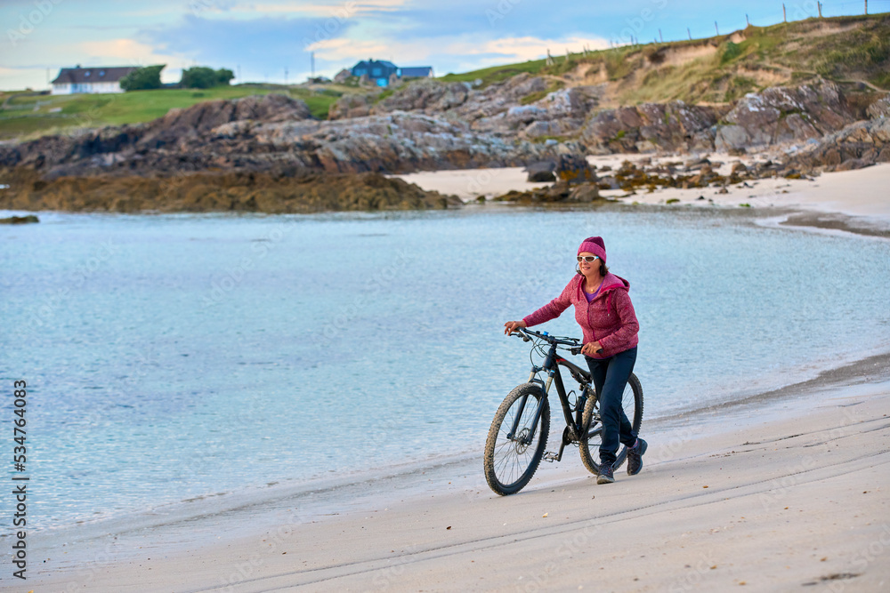 Fototapeta premium nice senior woman on mountain bike, cycling in sunset at the golden sand beach of Sillerna, Grallagh, County Galway, in the western part of the Republic of Ireland