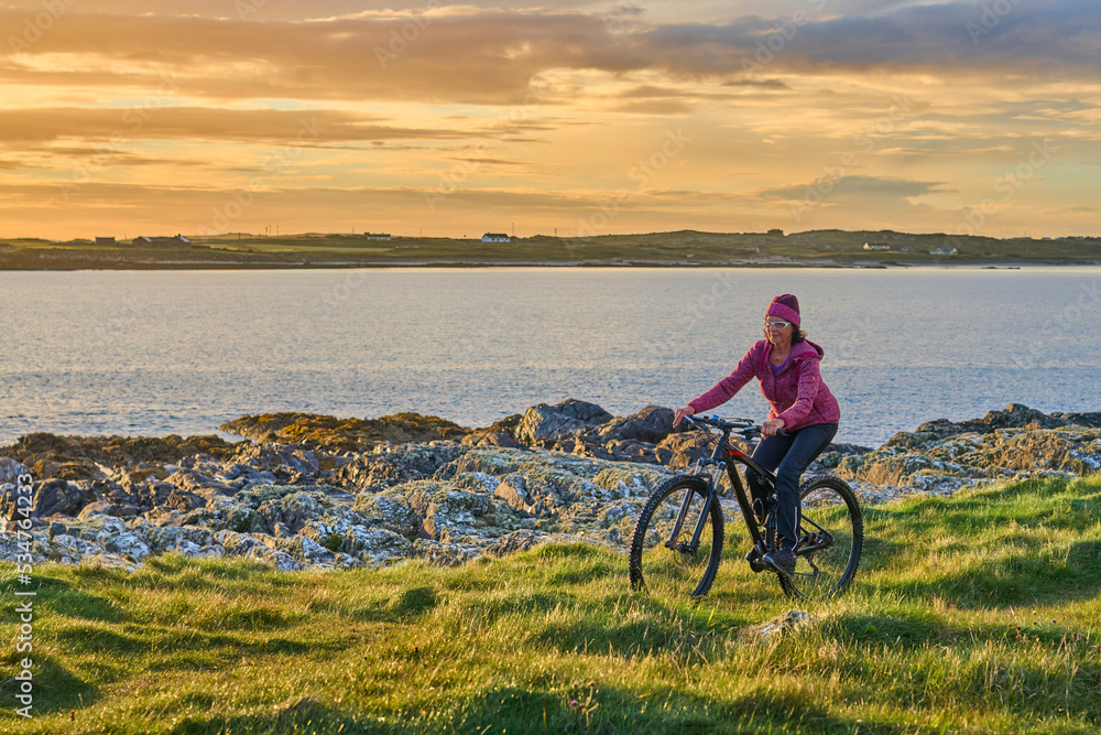 nice senior woman on mountain bike, cycling in sunset on the cliffs of Sillerna, Grallagh, County Galway, in the western part of the Republic of Ireland nice senior woman on mountain bike, cycling in sunset on the cliffs of Sillerna, Grallagh, County Galway, in the western part of the Republic of Ireland