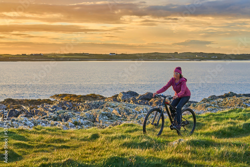 nice senior woman on mountain bike, cycling in sunset on the cliffs of Sillerna, Grallagh, County Galway, in the western part of the Republic of Ireland