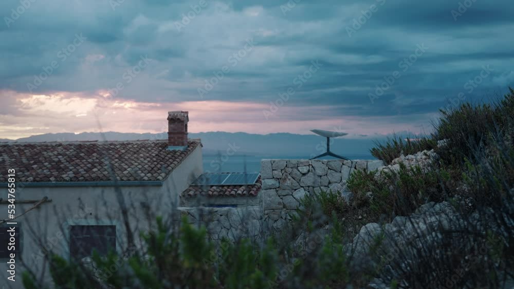 Starlink SpaceX Tesla satellite internet receiver dish on a fence of a rural home on a small island near the sea at sunset. Living off grid in a tiny home with a beautiful location. Solar panels. Starlink SpaceX Tesla satellite internet receiver dish on a fence of a rural home on a small island near the sea at sunset. Living off grid in a tiny home with a beautiful location. Solar panels.
