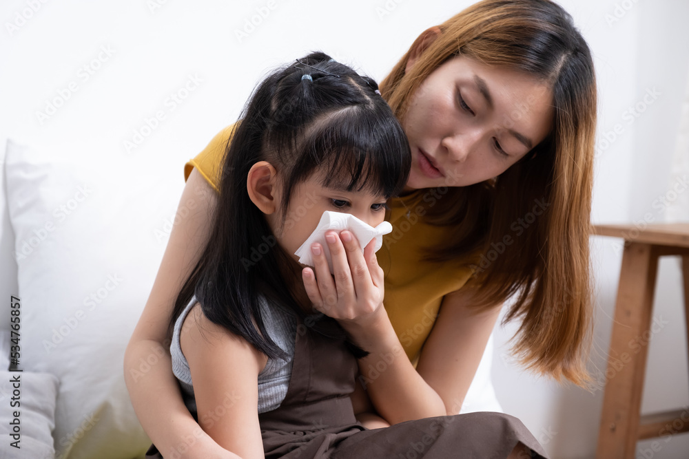 Close up shot of young Asian girl who has fever. that taking out mucus from nose and check body temperature by her mother inside of the bedroom. Sick and illness of young children, mother care.