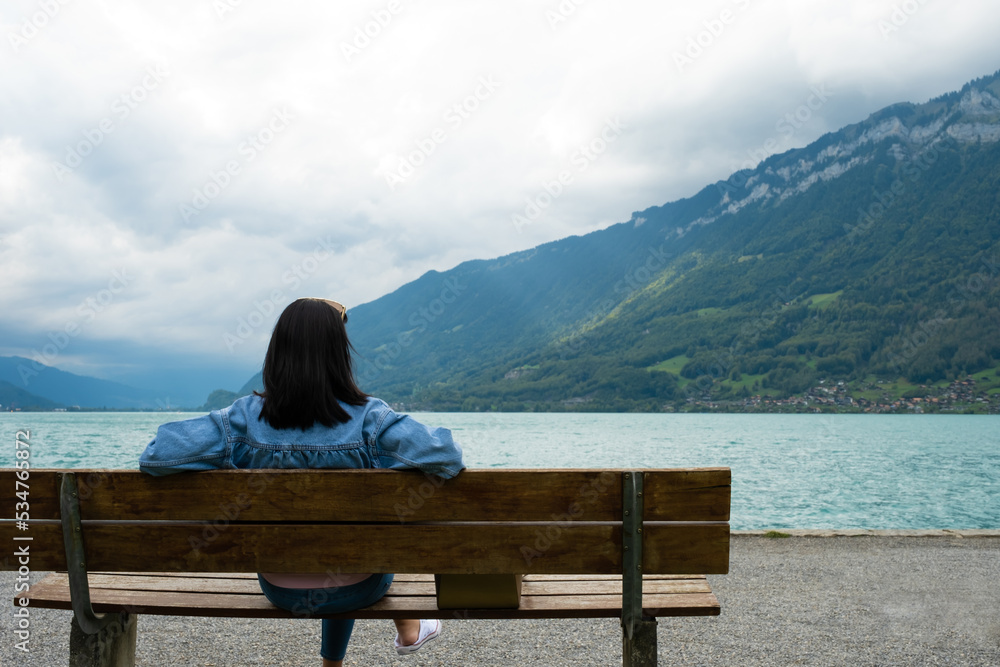 Young Asian tourist women sitting on a bench beside the lagoon while enjoy travel in Iseltwald Switzerland. Tourist attraction view point with copy space.