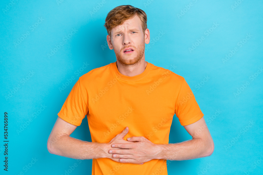 Photo of sick ginger hair guy stomachache wear orange t-shirt isolated on vivid blue color background Photo of sick ginger hair guy stomachache wear orange t-shirt isolated on vivid blue color background