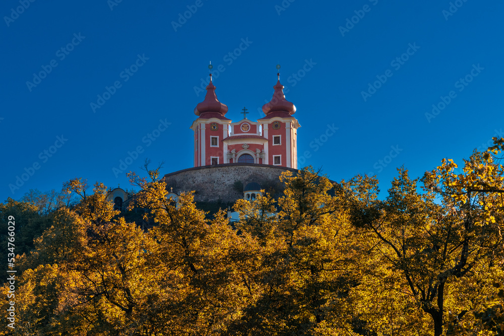 view of the red Calvary Banska Stiavnica under a blue sky with autumn forest in foreground