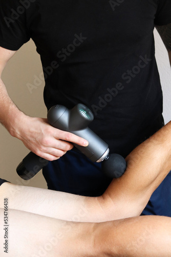 Sports percussion massage in medical room of gym. Masseur does massage exercises. Percussions therapy for regenerating massage of sport body. Concept of rehabilitation of sports injuries