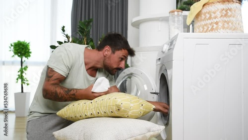 Young man has a laundry day at home, searching for the one lost socks in the washing machine. Guy cant find one sock after washing.