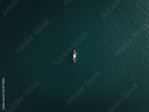 small canoe seen from a great height alone with two people inside in the middle of the lake areas with the brightness of the sun reflecting in the water, tarawera lake, new zealand photo