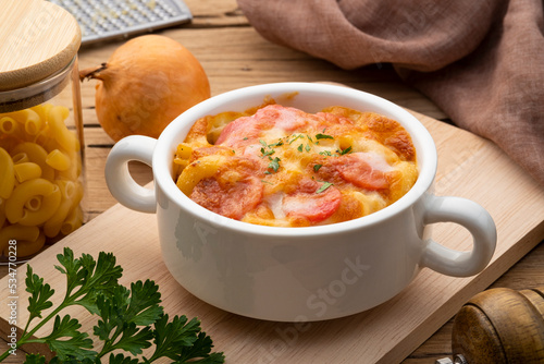 Baked macaroni with sausage and cheese with fresh parsley leaves in white bowl photo