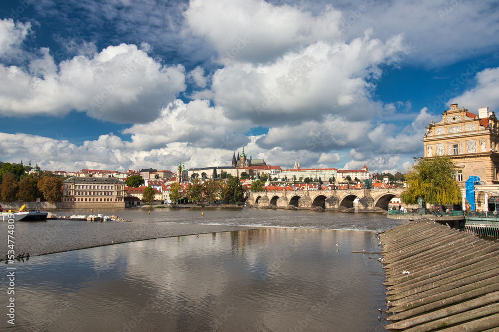 View over Vltava river to Charles bridge, Prague Castle in background under blue sky with white clouds.	