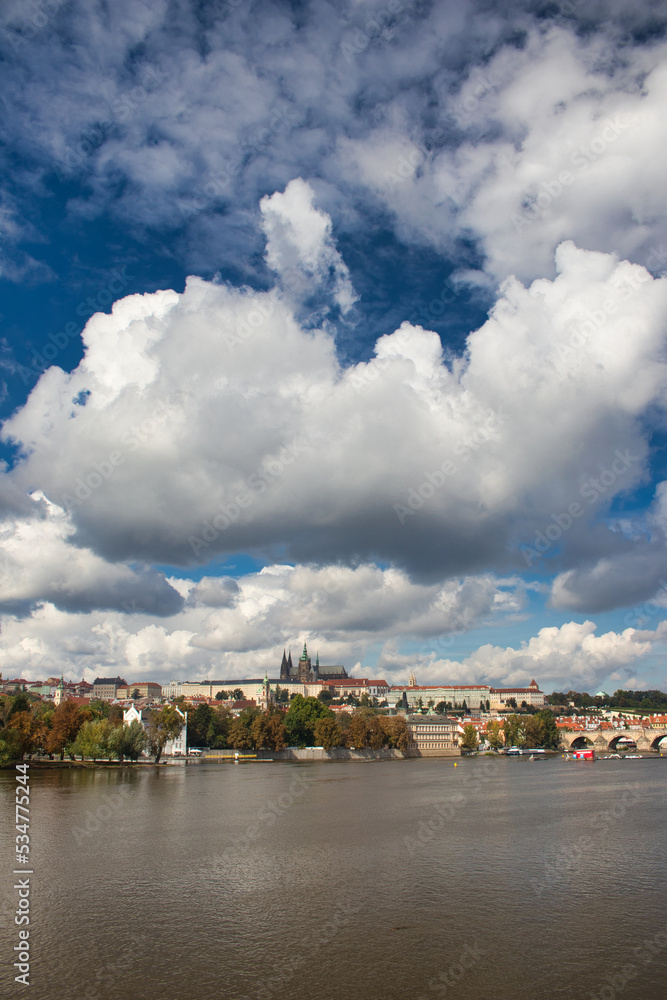 View over Vltava river to Charles bridge, Prague Castle in background under blus sky with white clouds.