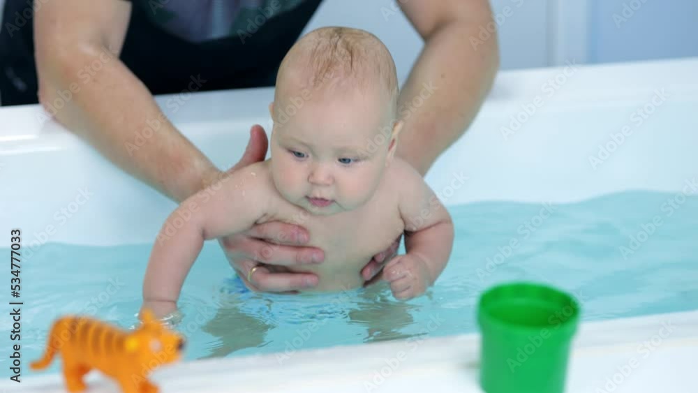 Baby girl with father help explores new things and bathes in bathtub with water. Girl with amused expression enjoys spending time with father Baby girl with father help explores new things and bathes in bathtub with water. Girl with amused expression enjoys spending time with father