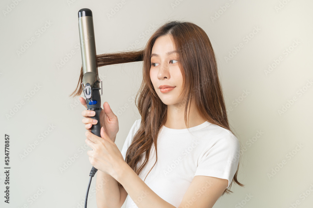Beautiful curly brunette, attractive asian young woman, girl smiling using curler, curling iron long hair with ceramic curler straightener at home. Hairstyle and Hairdressing. Beauty and hair care . Beautiful curly brunette, attractive asian young woman, girl smiling using curler, curling iron long hair with ceramic curler straightener at home. Hairstyle and Hairdressing. Beauty and hair care .