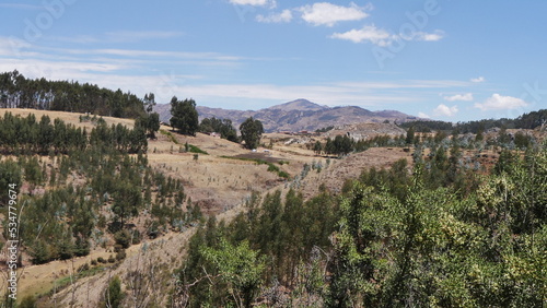 Un parc national péruvien naturel et bien entretenu, avec plaines, chemins de terre, montagnes rouges, petites forêts, sous un soleil de plomb, balade bien-être, parcours sportif