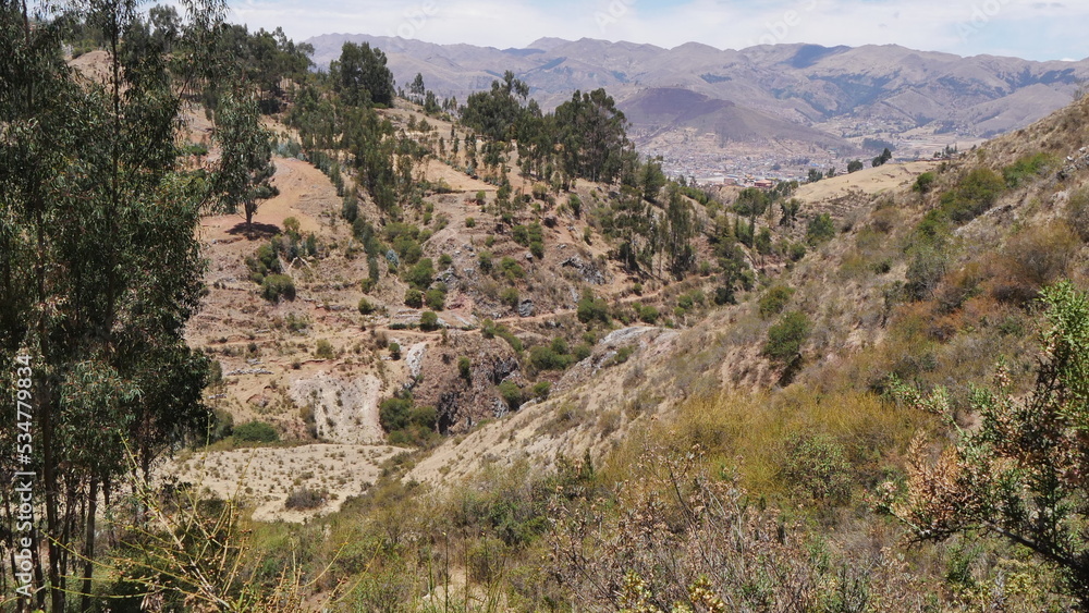 Un parc national péruvien naturel et bien entretenu, avec plaines, chemins de terre, montagnes rouges, petites forêts, sous un soleil de plomb, balade bien-être, parcours sportif