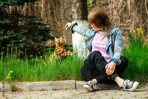 A beautiful girl sits on the ground and plays with her bright Bengal cat