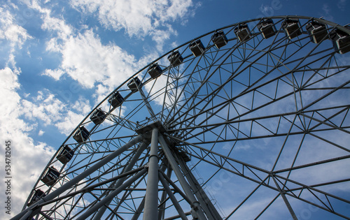 A new metal Ferris wheel with booths on the background of a blue cloudy sky in Vladimir Park Russia on a summer day and a space for copying