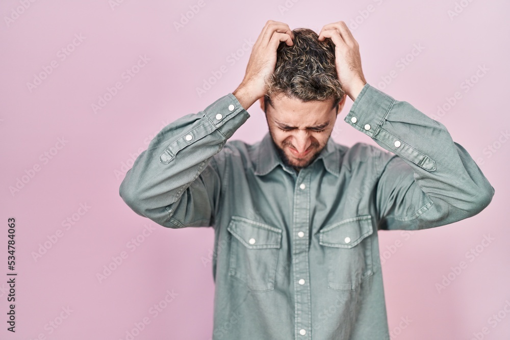 Hispanic man with beard standing over pink background suffering from headache desperate and stressed because pain and migraine. hands on head. Hispanic man with beard standing over pink background suffering from headache desperate and stressed because pain and migraine. hands on head.