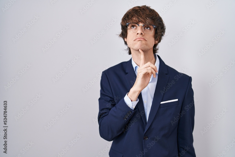 Hispanic business young man wearing glasses thinking concentrated about doubt with finger on chin and looking up wondering Hispanic business young man wearing glasses thinking concentrated about doubt with finger on chin and looking up wondering