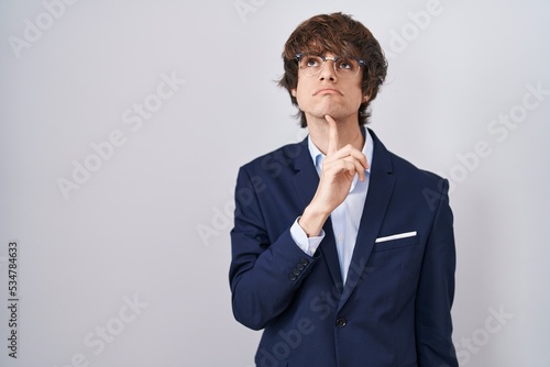 Hispanic business young man wearing glasses thinking concentrated about doubt with finger on chin and looking up wondering