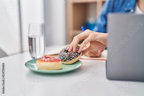 Young hispanic man holding donut studying at home