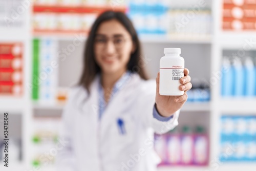 Young hispanic girl pharmacist holding pills at pharmacy