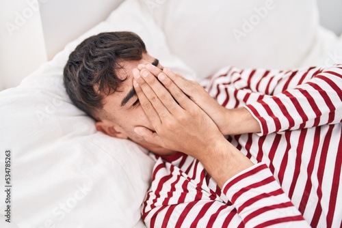 Young hispanic man stressed lying on bed at bedroom