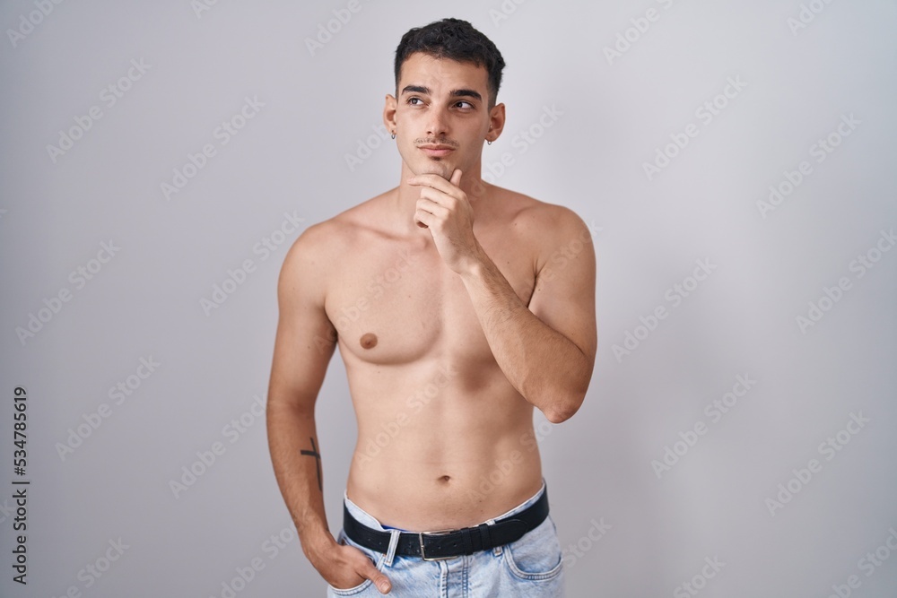 Handsome hispanic man standing shirtless with hand on chin thinking about question, pensive expression. smiling with thoughtful face. doubt concept.