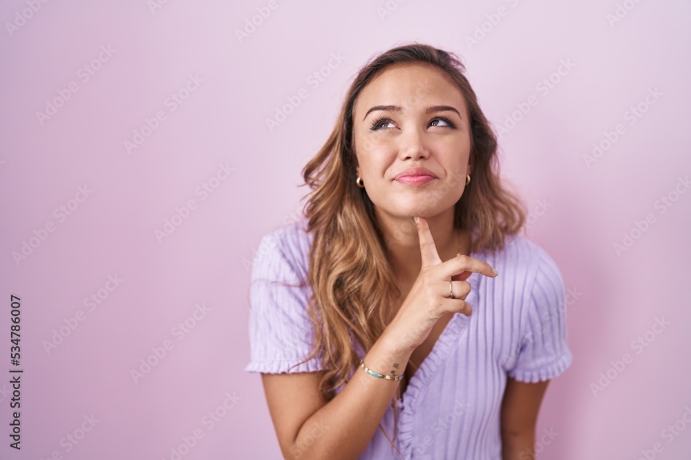Young hispanic woman standing over pink background thinking concentrated about doubt with finger on chin and looking up wondering Young hispanic woman standing over pink background thinking concentrated about doubt with finger on chin and looking up wondering