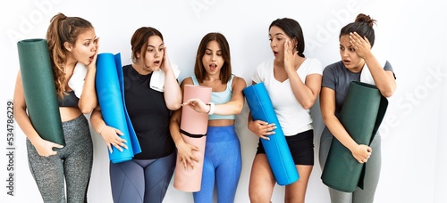 Group of women holding yoga mat standing over isolated background looking at the watch time worried, afraid of getting late