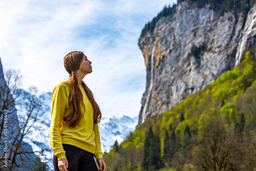 a cute woman in ponies enjoys the view in the alpine valley of lauterbrunnen in switzerland; a mountain valley surrounded by waterfalls and mighty peaks