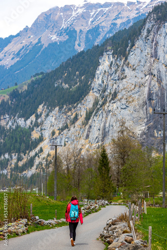 hiker girl with backpack walks through an alpine valley surrounded by mighty mountains and numerous waterfalls; valley walk in lauterbrunnen, swiss alps