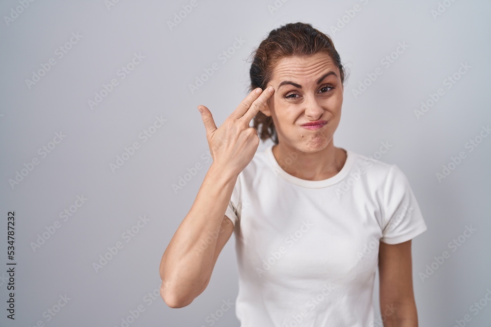Beautiful brunette woman standing over isolated background shooting and killing oneself pointing hand and fingers to head like gun, suicide gesture. Beautiful brunette woman standing over isolated background shooting and killing oneself pointing hand and fingers to head like gun, suicide gesture.