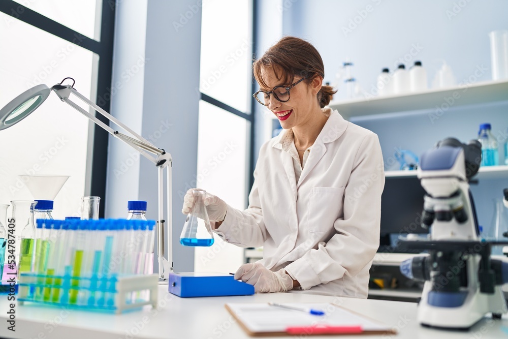 Young caucasian woman wearing scientist uniform measuring liquid at laboratory Young caucasian woman wearing scientist uniform measuring liquid at laboratory