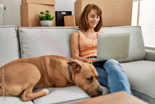 Young caucasian woman having video call sitting on sofa with dog at home