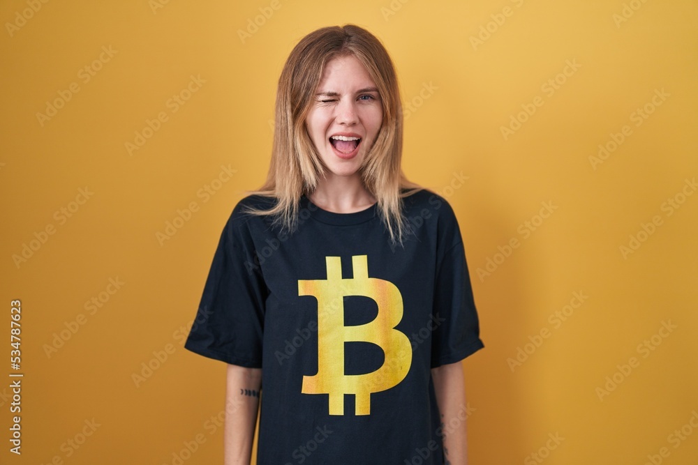Blonde caucasian woman wearing bitcoin t shirt winking looking at the camera with sexy expression, cheerful and happy face. Blonde caucasian woman wearing bitcoin t shirt winking looking at the camera with sexy expression, cheerful and happy face.