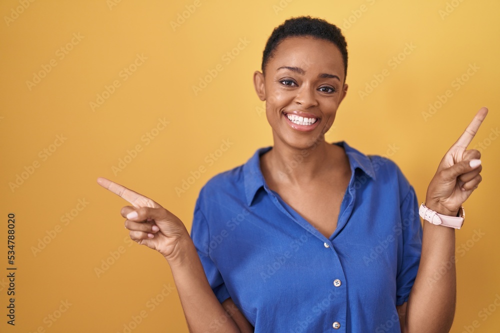 African american woman standing over yellow background smiling confident pointing with fingers to different directions. copy space for advertisement African american woman standing over yellow background smiling confident pointing with fingers to different directions. copy space for advertisement