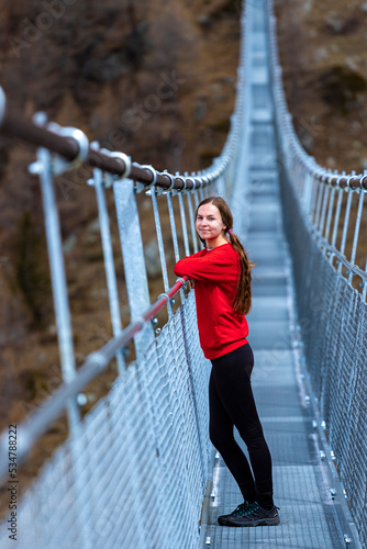 Cute girl in pigtails standing on the world's longest suspension bridge - Charles Kuonen Suspension Bridge; hiking in the mountains; view of mighty snowy alpine peaks, switzerland