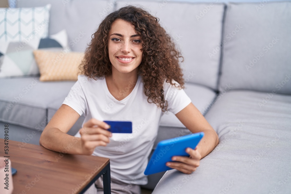 Young beautiful hispanic woman using touchpad and credit card sitting on floor at home Young beautiful hispanic woman using touchpad and credit card sitting on floor at home