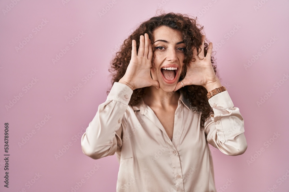 Hispanic woman with curly hair standing over pink background smiling cheerful playing peek a boo with hands showing face. surprised and exited Hispanic woman with curly hair standing over pink background smiling cheerful playing peek a boo with hands showing face. surprised and exited