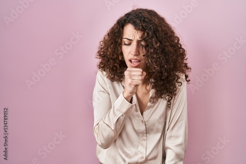 Hispanic woman with curly hair standing over pink background feeling unwell and coughing as symptom for cold or bronchitis. health care concept. © Krakenimages.com