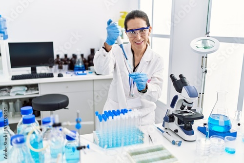 Young hispanic woman wearing scientist uniform using pipette at laboratory