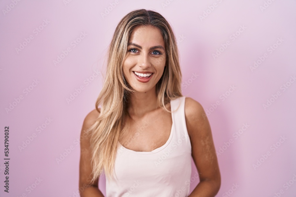 Young blonde woman standing over pink background with hands together and crossed fingers smiling relaxed and cheerful. success and optimistic Young blonde woman standing over pink background with hands together and crossed fingers smiling relaxed and cheerful. success and optimistic