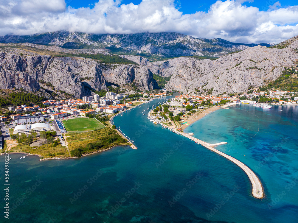 aerial view of the town of omiš in croatia, a picturesque town on the adriatic coast with the mouth of the cetina river, a beautiful beach and mighty mountains in the background as seen from a drone