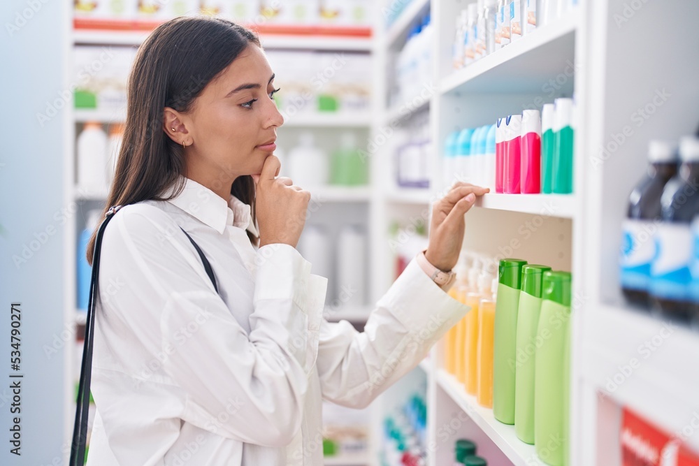 Young beautiful hispanic woman client holding toothpaste at pharmacy