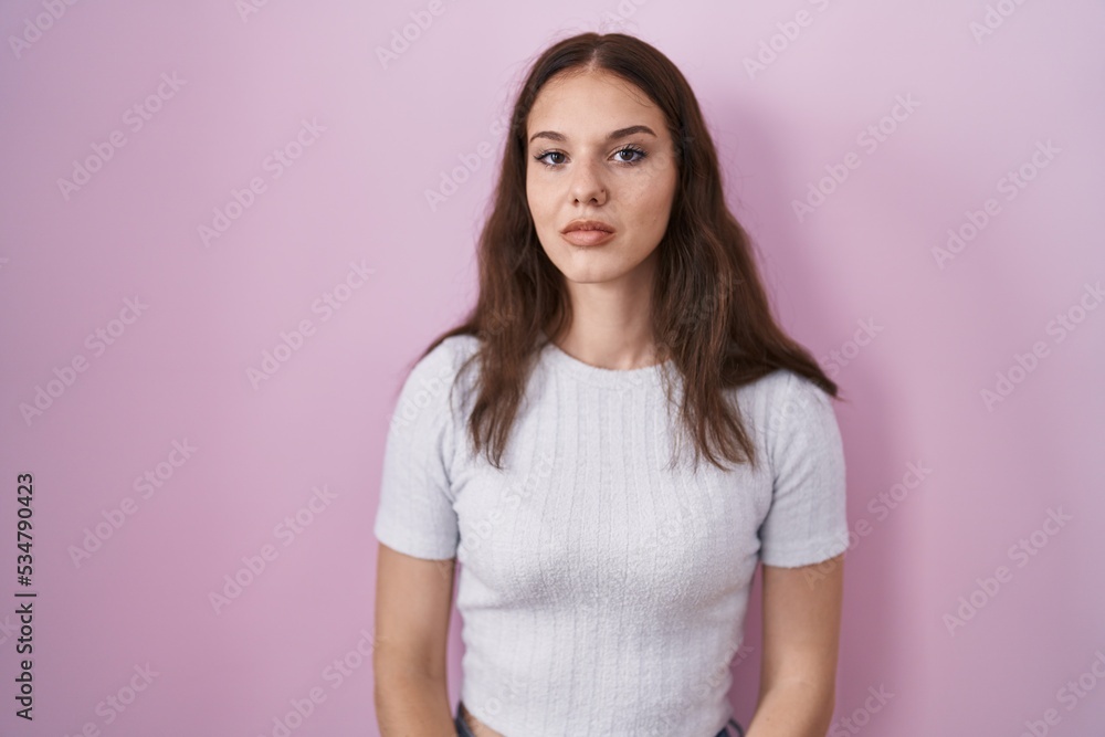 Young hispanic girl standing over pink background relaxed with serious expression on face. simple and natural looking at the camera. Young hispanic girl standing over pink background relaxed with serious expression on face. simple and natural looking at the camera.