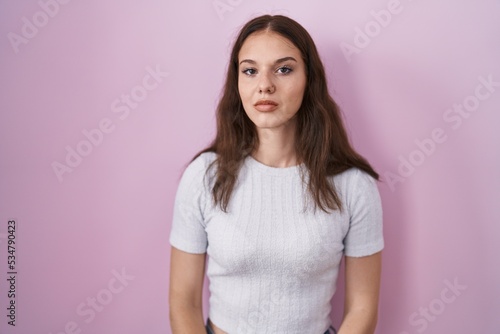 Young hispanic girl standing over pink background relaxed with serious expression on face. simple and natural looking at the camera.