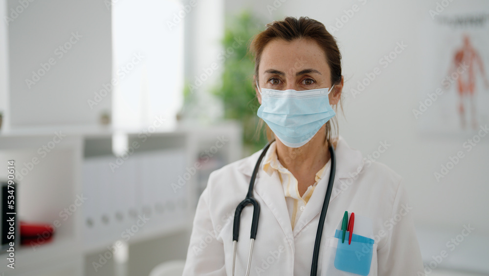 Middle age hispanic woman wearing doctor uniform and medical mask at clinic Middle age hispanic woman wearing doctor uniform and medical mask at clinic