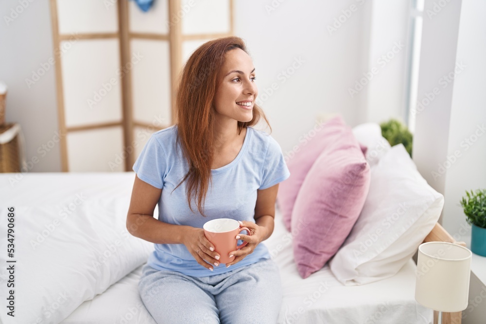 Young woman drinking cup of coffee sitting on bed at bedroom Young woman drinking cup of coffee sitting on bed at bedroom