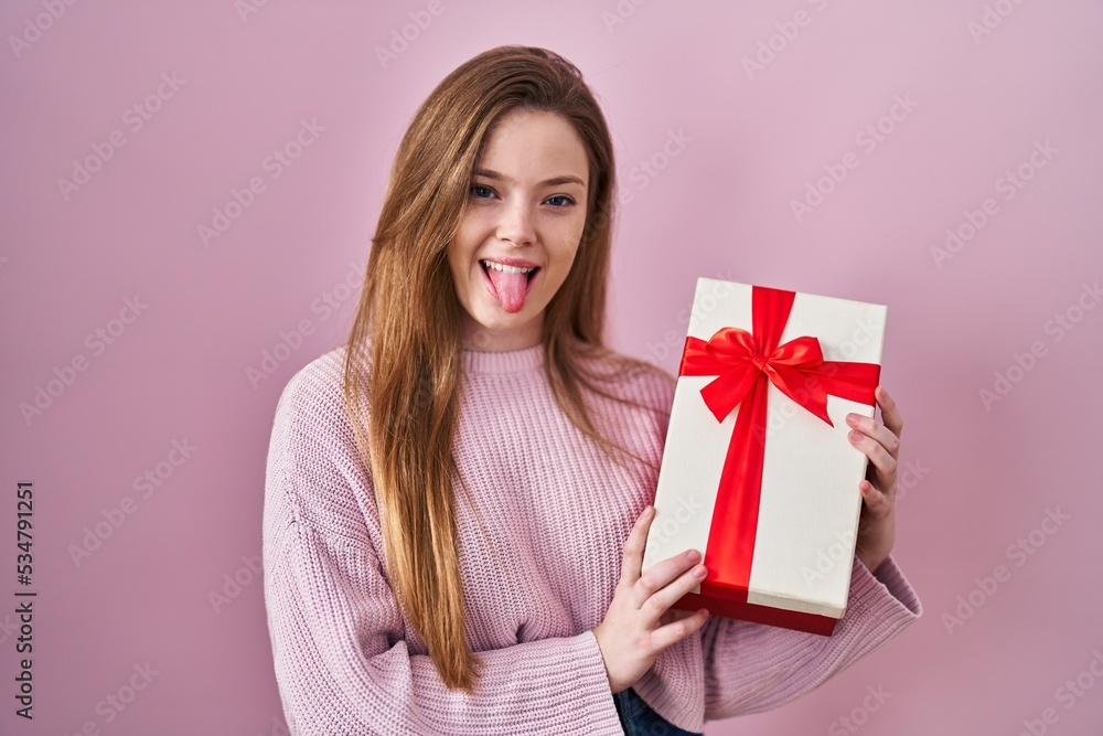 Young caucasian woman holding gift sticking tongue out happy with funny expression. Young caucasian woman holding gift sticking tongue out happy with funny expression.